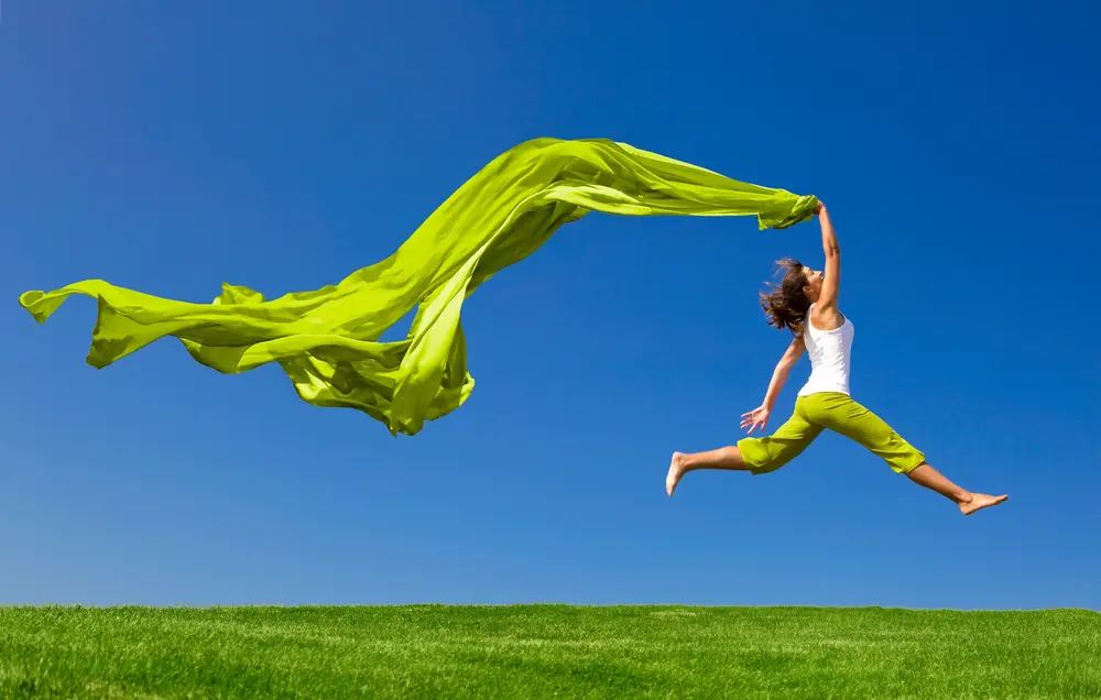 Junge Frau springt mit einem grünen Tuch über eine grüne Wiese – © Fotolia